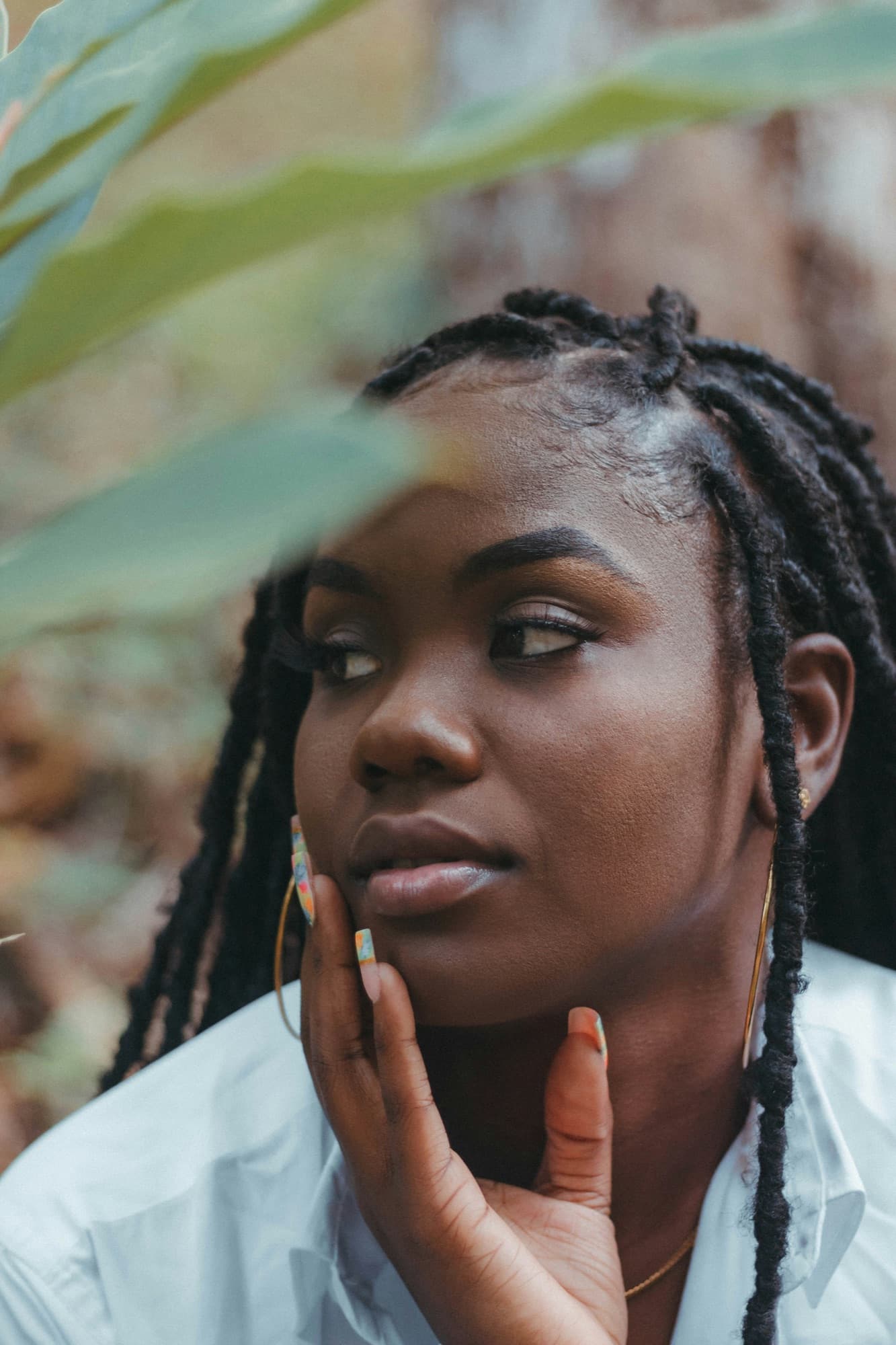 Woman with locs and painted nails, her hand on her cheek