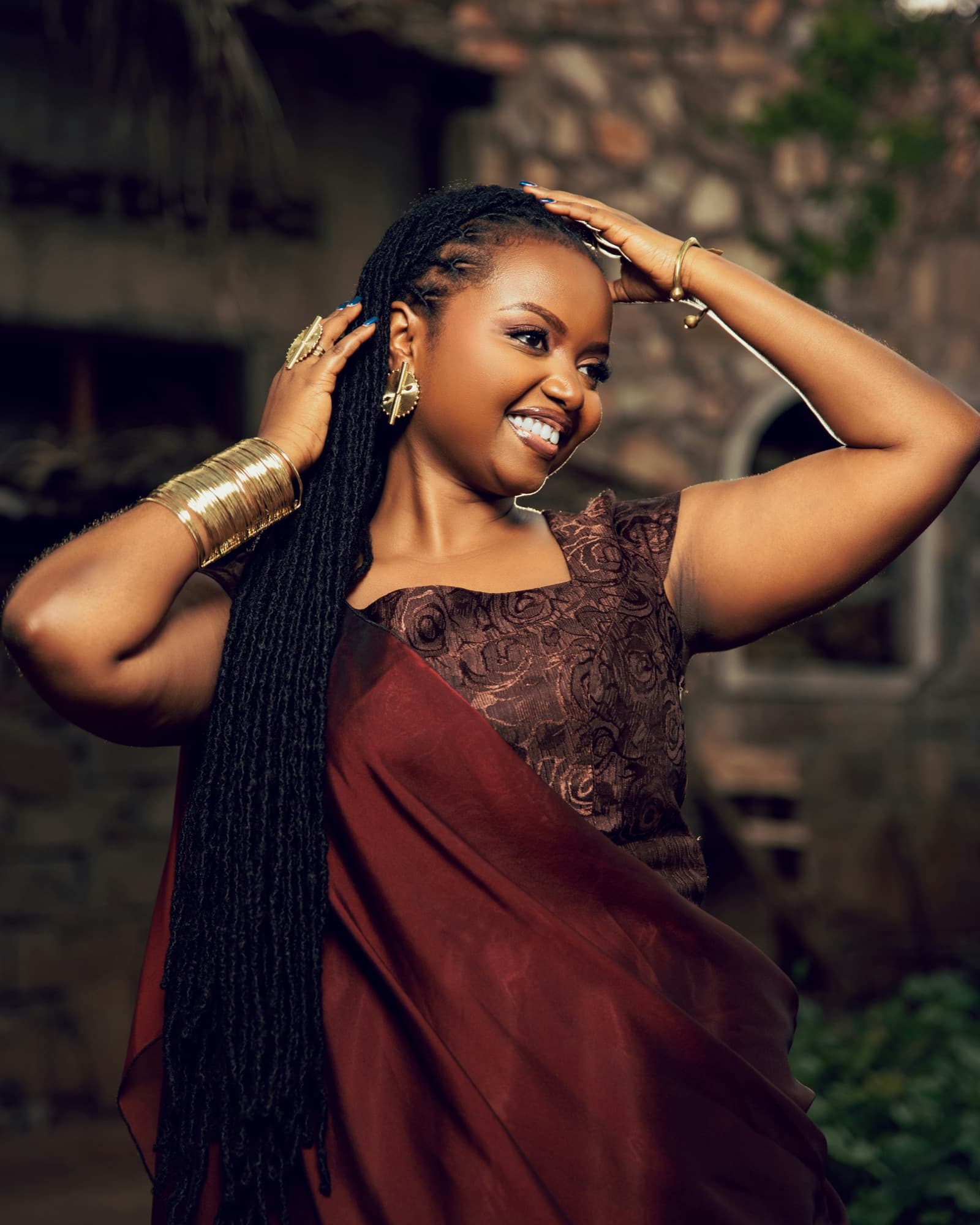 Smiling woman with long locs, her hands in her hair